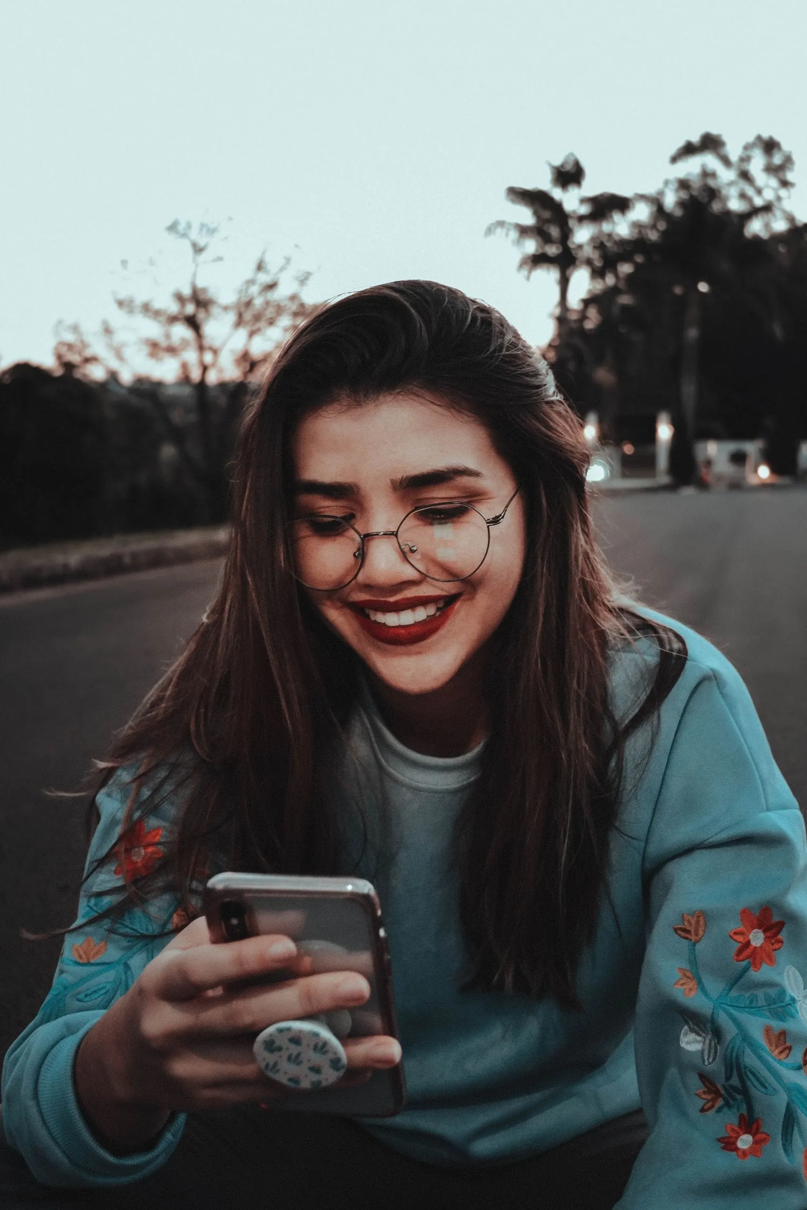 A woman smiling at her phone outdoors at dusk